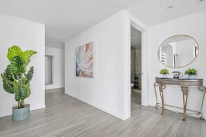 A modern interior with a wooden floor, a large abstract painting, a round mirror, and a potted plant.