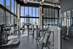 A gym with various exercise equipment, large windows, and a view of the city skyline.