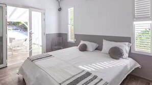 A bedroom with a bed, a chair, a window, and a door leading to an outdoor area.