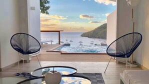 A balcony with a view of the sea and boats, two blue chairs, a glass table, and a sofa.