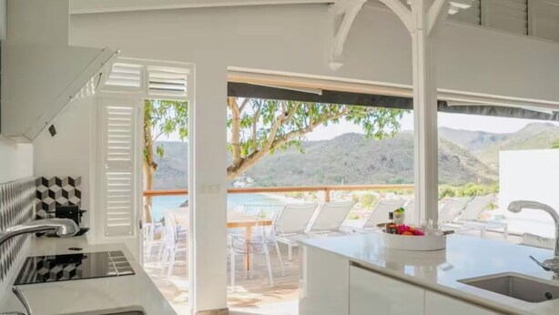 A modern kitchen with white cabinetry, a built-in stove, and a large window overlooking a deck with outdoor seating.