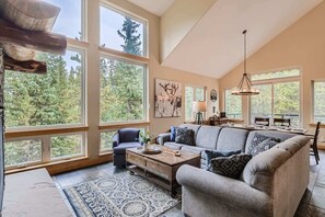 A spacious living room with large windows, a sectional sofa, a coffee table, and a dining area.