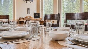 Una mesa de comedor dispuesta con platos, tazones y vasos, con una vista panorámica a través de la ventana.