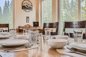 A dining table set with plates, bowls, and glasses, with a scenic view through the window. - Twin Creek Lodge (Breckenridge)