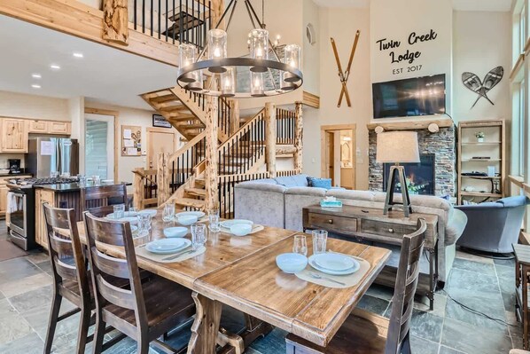 A spacious kitchen with a wooden island, a dining area with a wooden table set for four, and a staircase with a wooden railing.