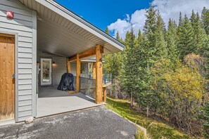 A wooden porch with a covered seating area, a garage door, and a view of a forested area.