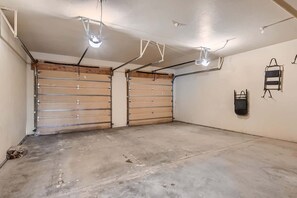 A garage with two large garage doors, concrete floor, and ceiling lights.