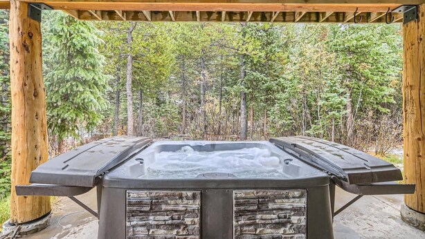 A hot tub under a wooden pergola with a forest backdrop.
