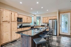 A modern kitchen with wooden cabinets, a central island with bar stools, stainless steel appliances, and a large window providing natural light.