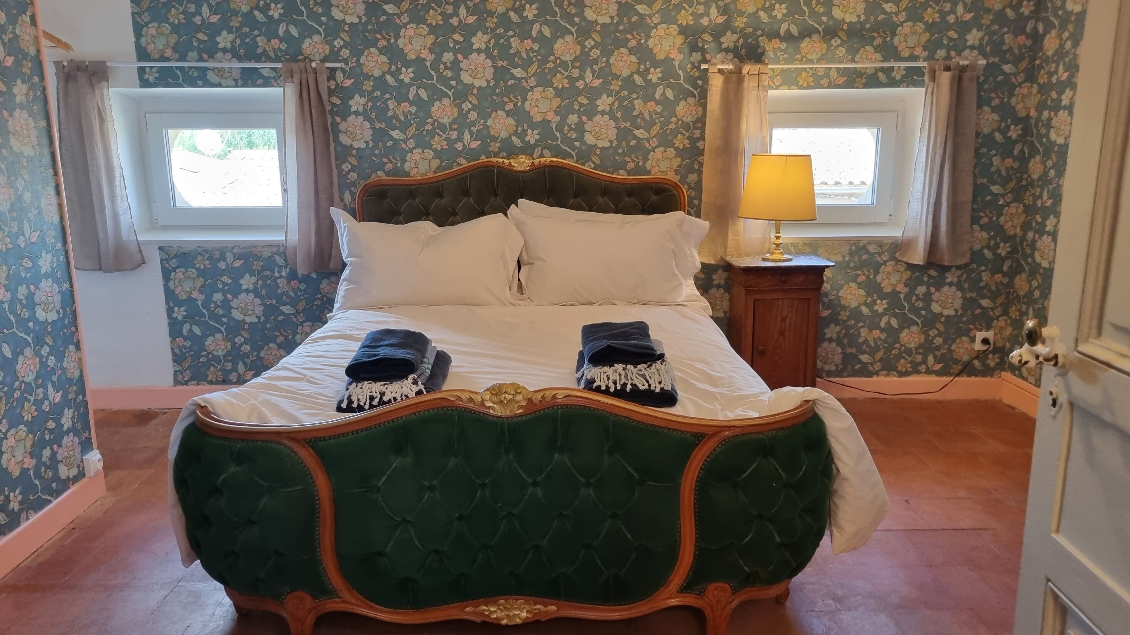 A bed with a green upholstered headboard, white bedding, and two folded towels.