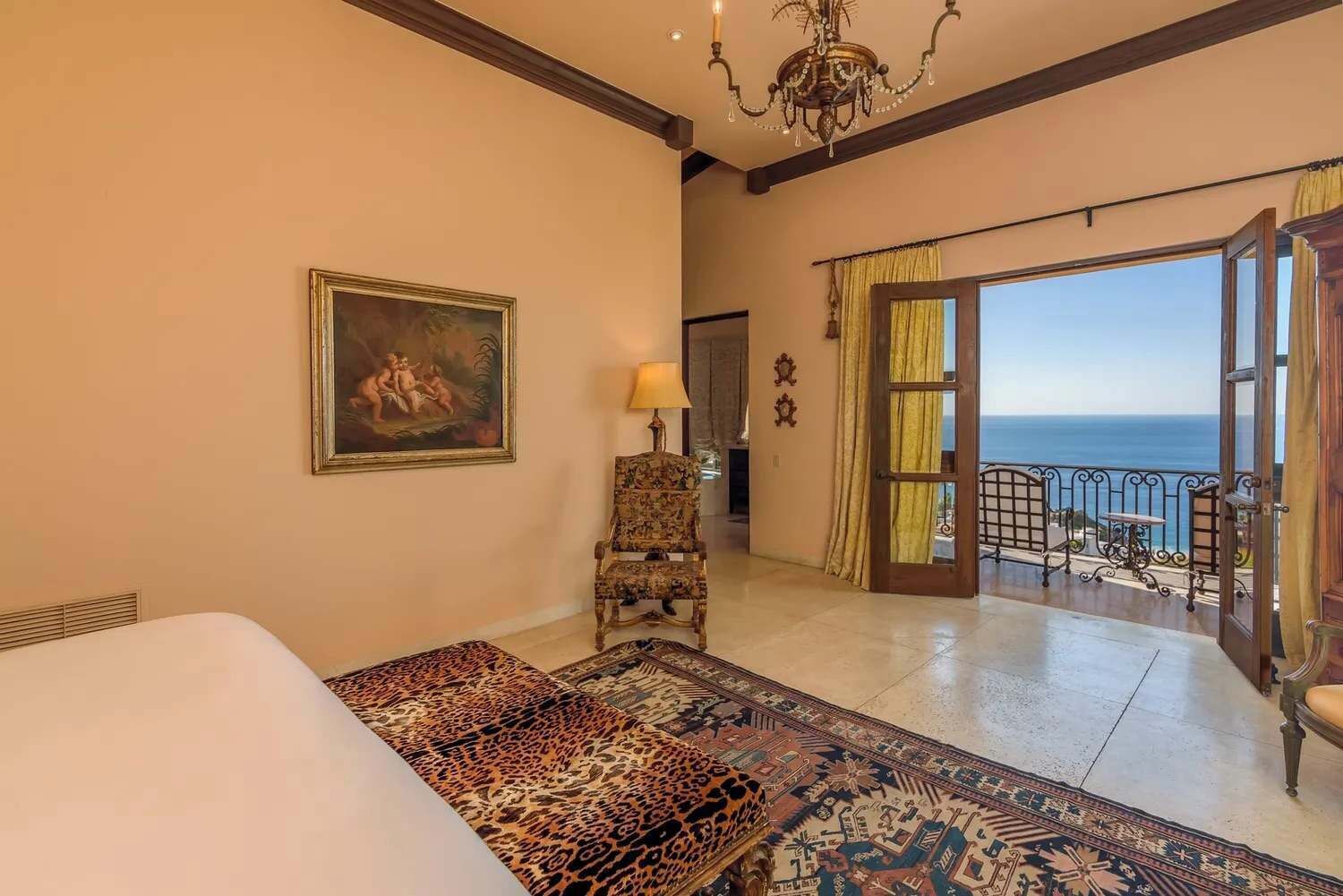A bedroom with a bed, a chair, a painting, a lamp, and a balcony with a view.