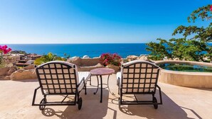 Two outdoor chairs facing a pool with a view of the sea.