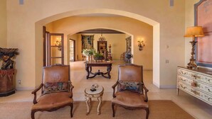A spacious living area with two leather armchairs, a round table, and a decorative fireplace.