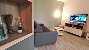 Ein modernes Wohnzimmer mit einem grauen Sofa, einem kleinen weißen Tisch und einem Fernseher auf einem Holzboden.