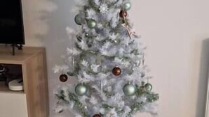 Ein kleiner, weißer Weihnachtsbaum mit Dekorationen, platziert in einem Raum mit Holzboden und einem Fernseher auf einem Holztisch.