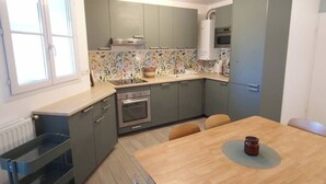 Eine kompakte Küche mit grauen Schränken, einer gefliesten Spritzschutzwand, einem Einbauofen und einem Esstisch mit Stühlen.