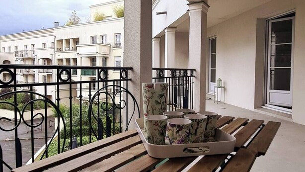 Ein Balkon mit einem Holztisch, einer Ablage mit bemalten Tassen und Blick auf Wohnhäuser.