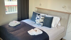 Una cama bien hecha con colcha azul oscuro, sábanas blancas y almohadas decorativas.