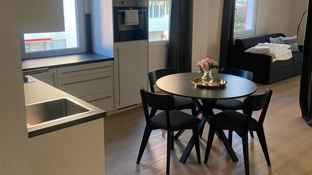 Una cocina moderna con comedor, que incluye una mesa redonda con sillas, horno empotrado y una ventana con cortinas.
