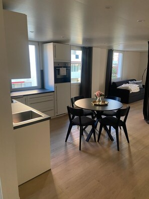 Una cocina moderna con comedor, que incluye una mesa redonda con sillas, horno empotrado y una ventana con cortinas.