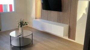 Una sala de estar moderna con una televisión de pantalla plana montada en una pared de listones, una mesa de centro redonda de cristal y un banco blanco.