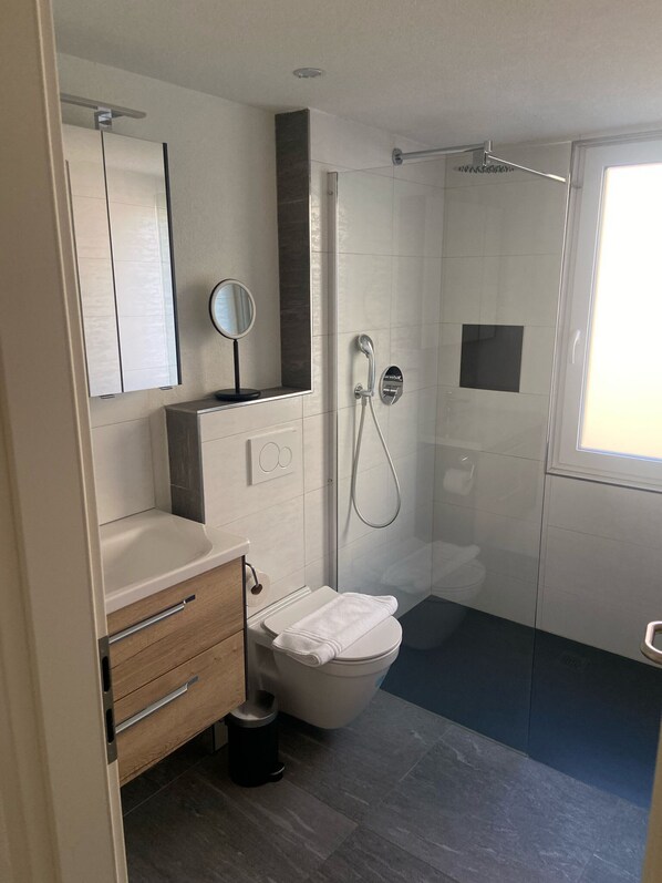 Un baño moderno con inodoro, lavamanos, tocador y ducha con mampara de vidrio.