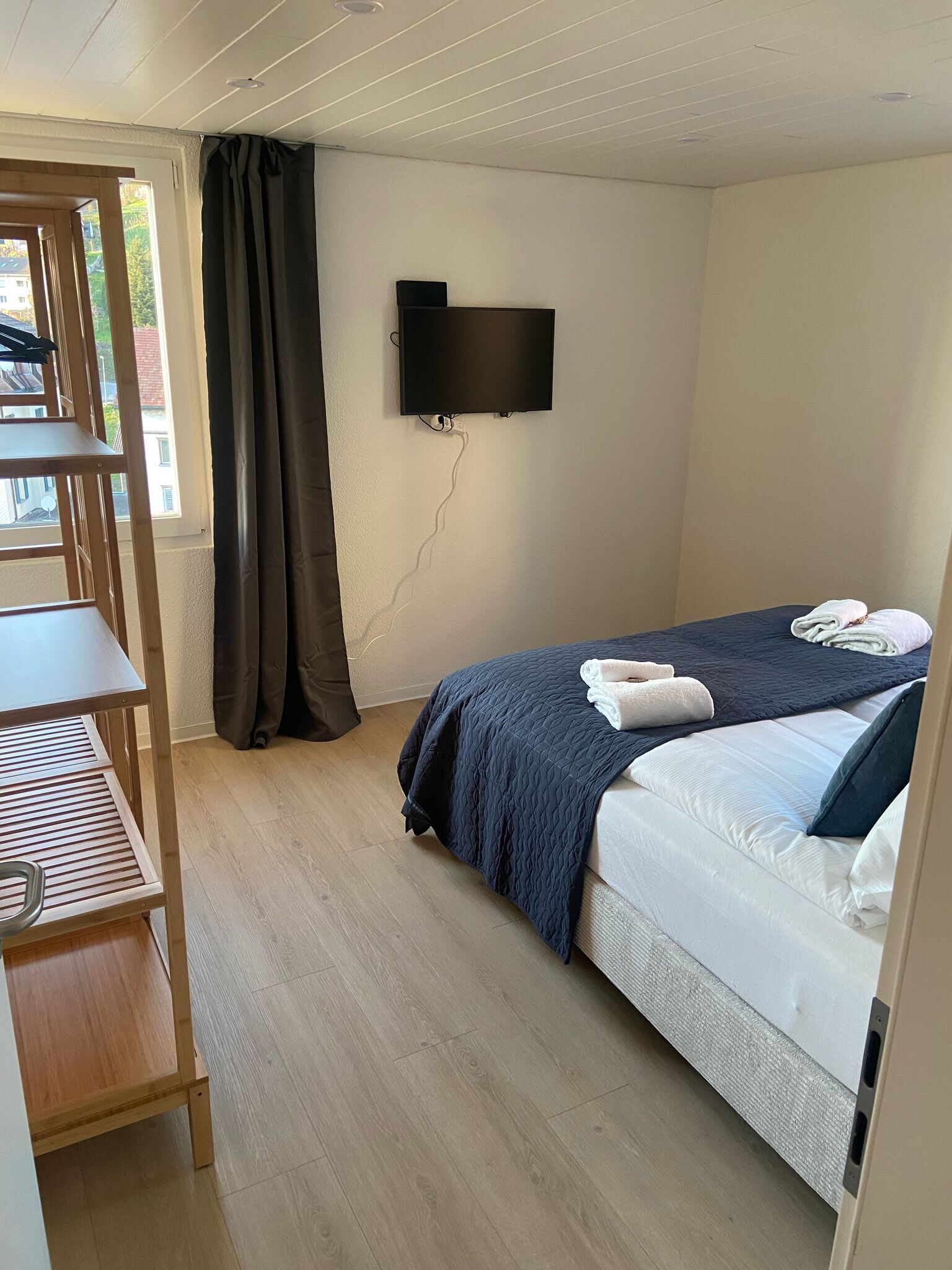 Una habitación pequeña y ordenada con una cama, un escritorio y un televisor montado en la pared.