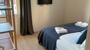Una habitación pequeña y ordenada con una cama, un escritorio y un televisor montado en la pared.