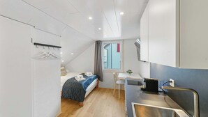 A compact room with a bed, a small desk, and a kitchenette. - book2sty: Cozy Studio with kitchenette and washing machine (Herisau)