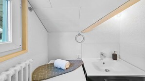 A small, modern bathroom with a white sink, a towel, and a wooden ceiling beam. - book2sty: Cozy Studio with kitchenette and washing machine (Herisau)