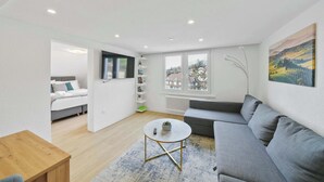 A modern living room with a grey sofa, a round coffee table, and a view of a cityscape through large windows.