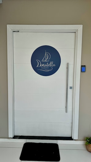 Une porte blanche ornée d’un logo circulaire sur lequel on peut lire « Donatella Pousada » et dotée d’une poignée.