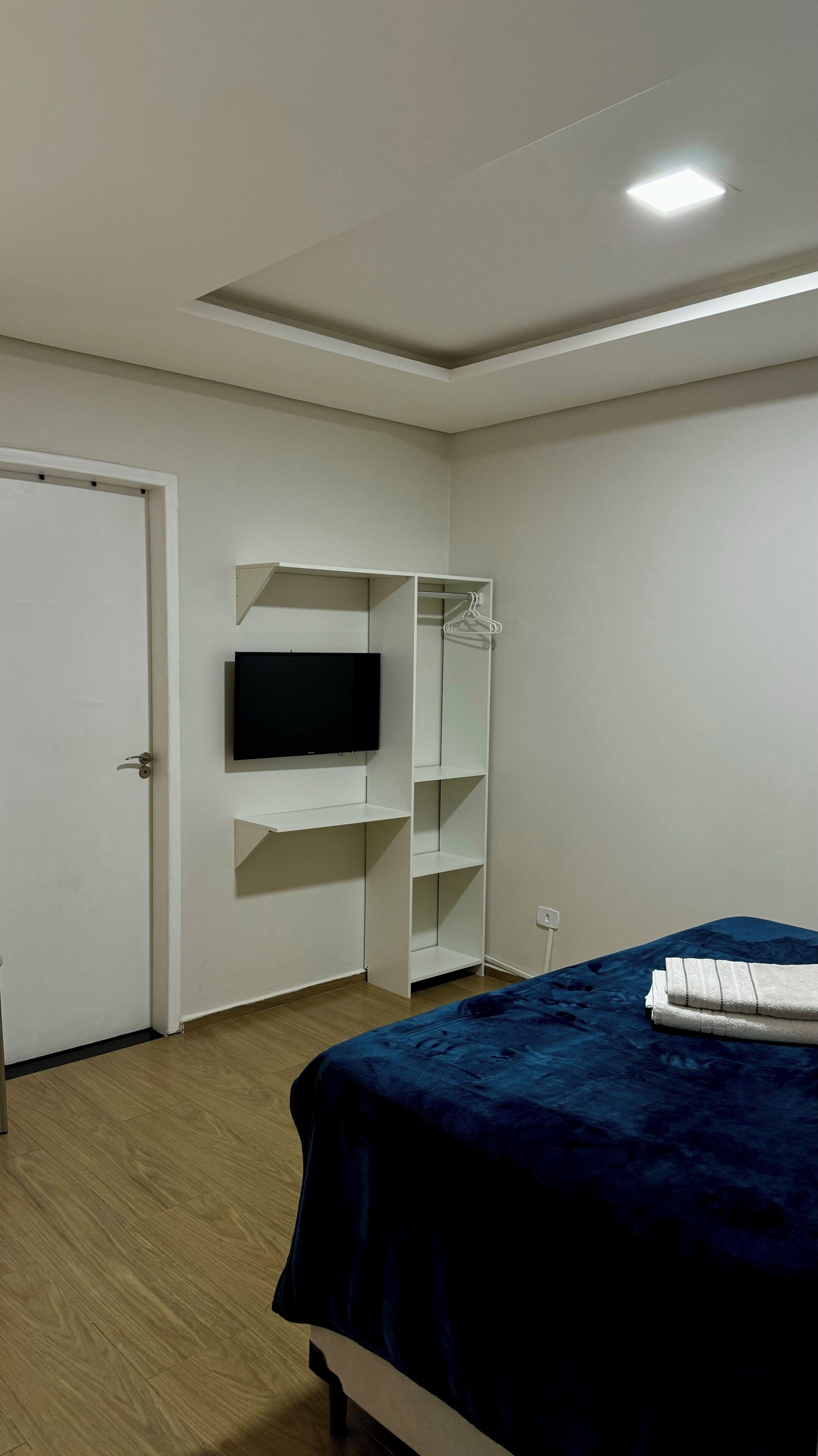 Un dormitorio con una cama, un televisor en la pared, un armario y una puerta.