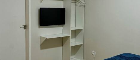 Un dormitorio con una cama, un televisor en la pared, un armario y una puerta.