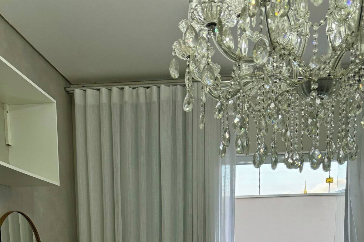 A hotel room with a bed, a small refrigerator, a mirror, and a chandelier.