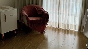 Ein Zimmer mit Holzboden, einem weißen Schreibtisch, einem roten Stuhl und einem großen Fenster mit durchsichtigen Vorhängen.