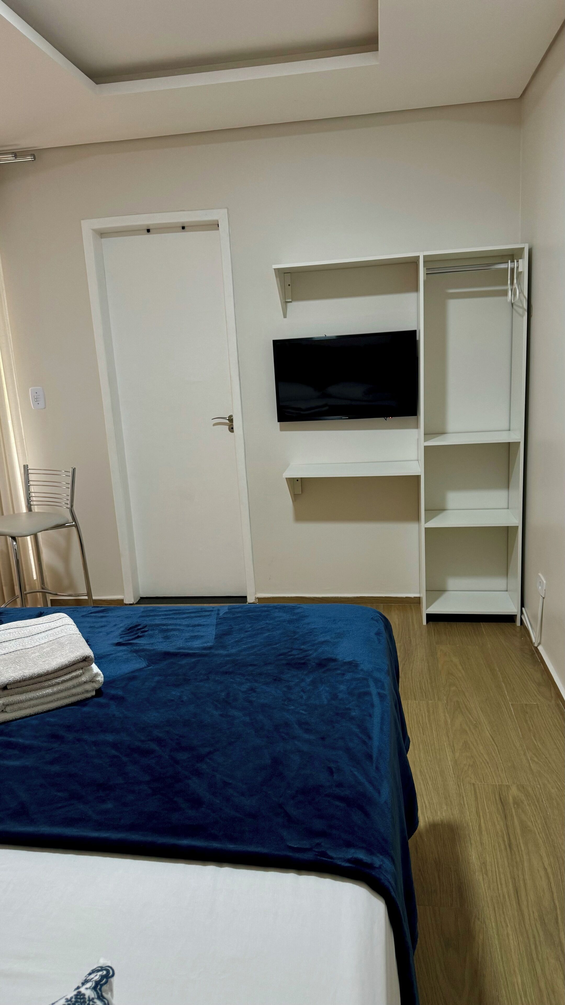 A bedroom with a bed, a TV mounted on the wall, a wardrobe, and a chair.