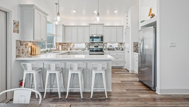 Une cuisine moderne avec des meubles blancs, un grand îlot central doté de tabourets, des appareils en acier inoxydable et un plancher en bois.