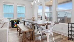 Un vaste espace dédié à la salle à manger, avec une table en bois, des chaises blanches et une vue sur l’extérieur grâce à de grandes fenêtres.