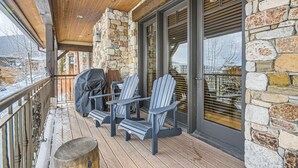 A covered outdoor seating area with Adirondack chairs and a grill, stone walls, and a view of the surrounding area.