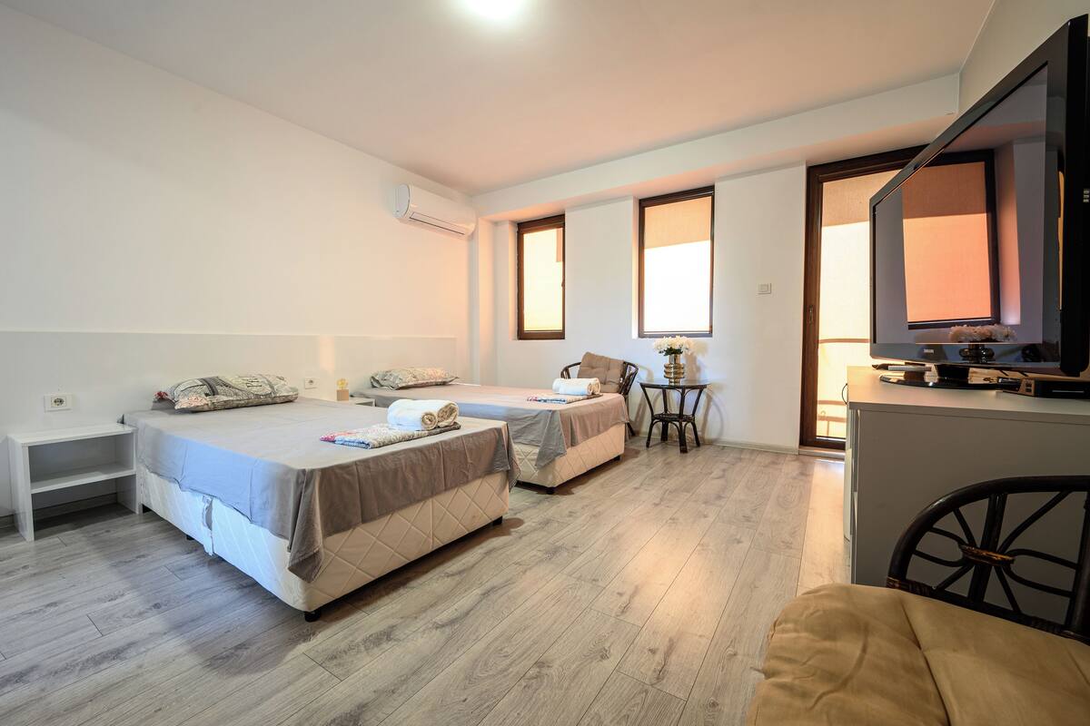 A hotel room with two beds, a desk, a small table with a lamp, and a television.