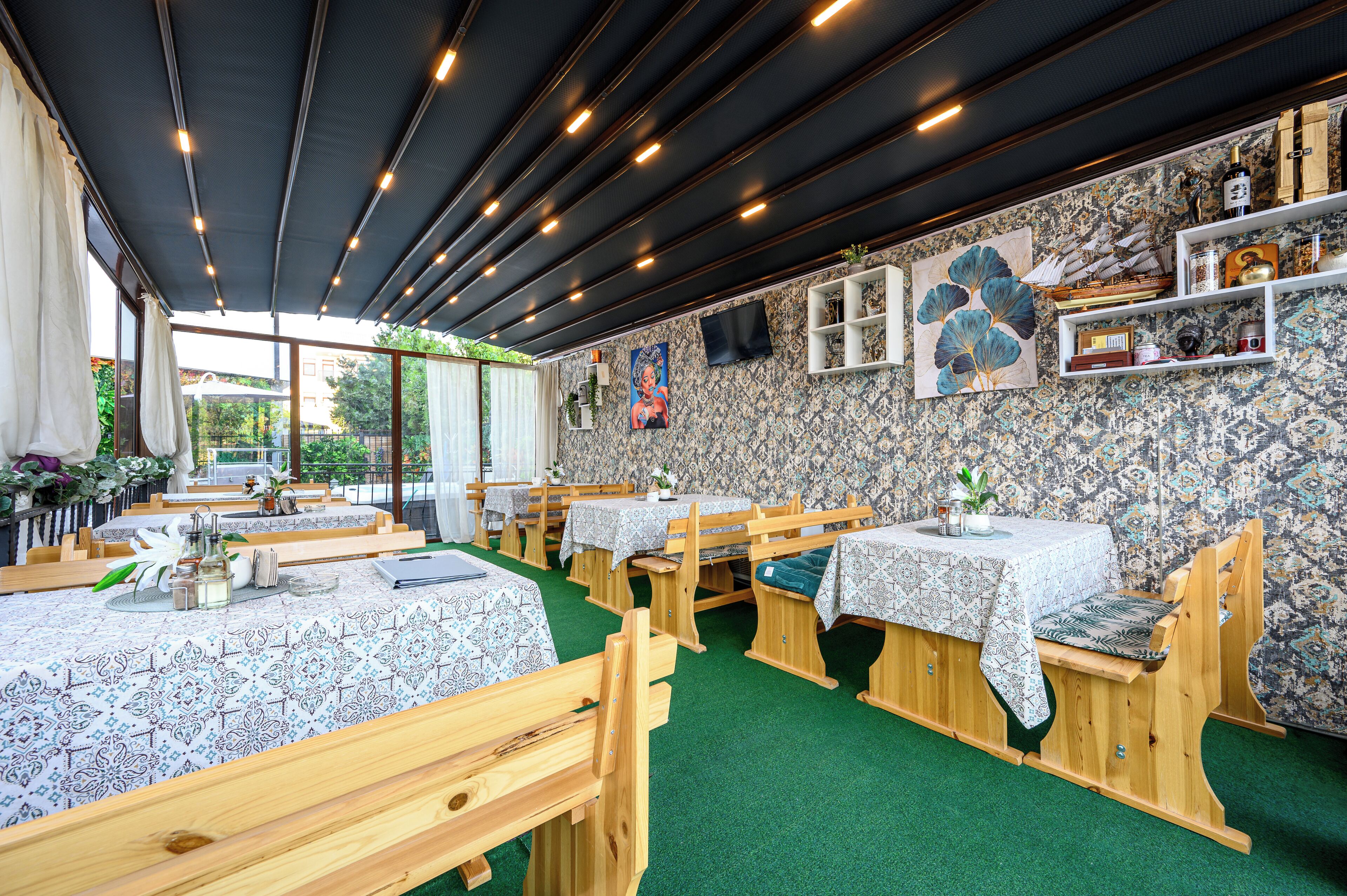 Een restaurant met houten banken en tafels, behang met een patroon en een groen tapijt.