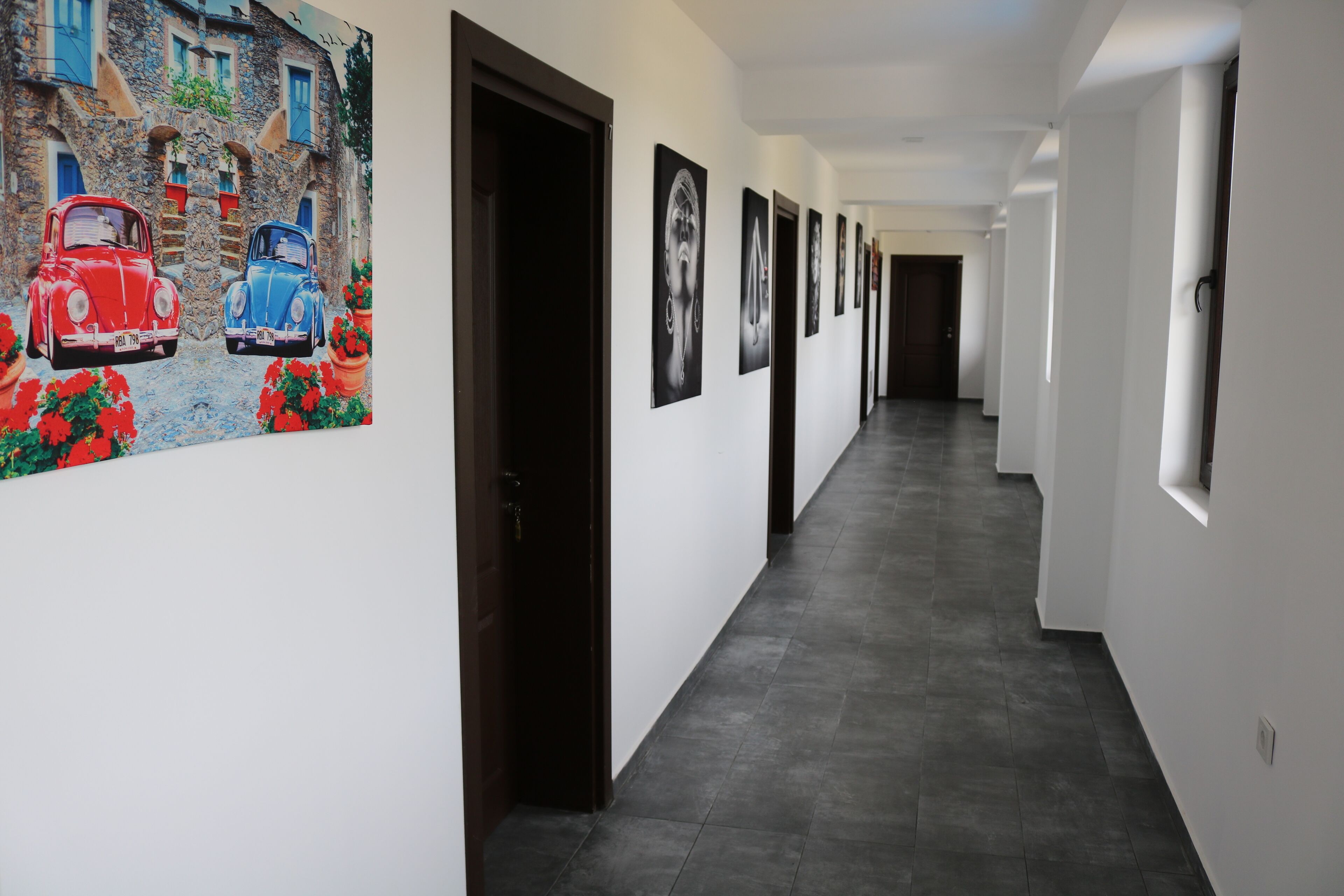 A hallway with a series of doors, each leading to a room. The walls are adorned with framed artwork, and the floor is tiled.