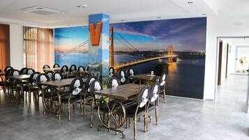 Un restaurant doté d’une grande fresque représentant un pont, de tables et de chaises en bois, et d’un décor intérieur moderne.