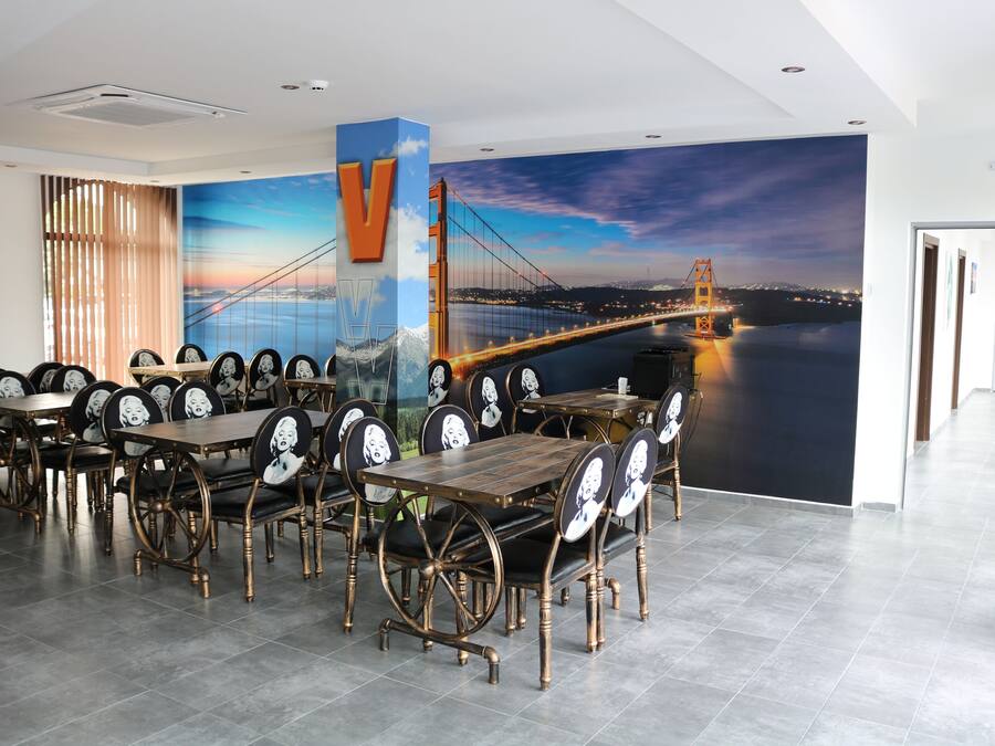 Un restaurant doté d’une grande fresque représentant un pont, de tables et de chaises en bois, et d’un décor intérieur moderne.