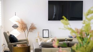 A modern living room with a flat-screen TV mounted on the wall, a sofa, a coffee table, and decorative plants. - Maroubra Gem Close to Beach Sleep 16 (Maroubra)