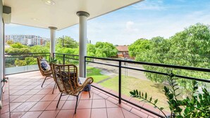 A balcony with a wicker chair, a view of a green landscape, and a tiled floor. - Maroubra Gem Close to Beach Sleep 16 (Maroubra)
