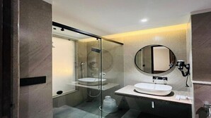 Un baño moderno con cabina de ducha de vidrio, un espejo redondo y dos lavamanos.