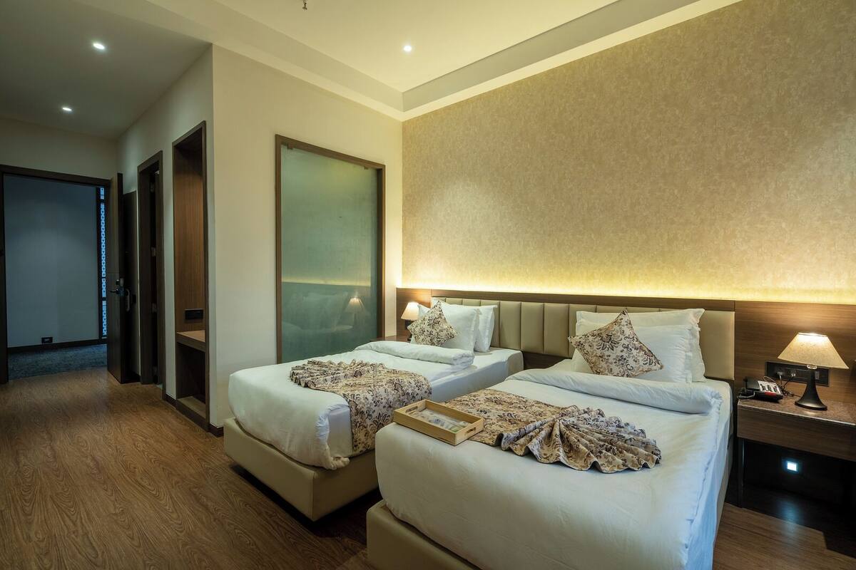 Een hotelkamer met twee bedden, een houten vloer, een grote spiegel en een nachtkastje met lamp.