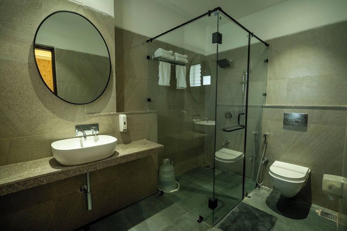 Een moderne badkamer met een douchecabine van glas, een ronde spiegel en een wit wastafelmeubel.